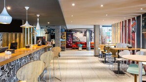 A modern interior with a bar area, seating, and a stage with a red couch. - ibis Bilbao Barakaldo (Barakaldo)