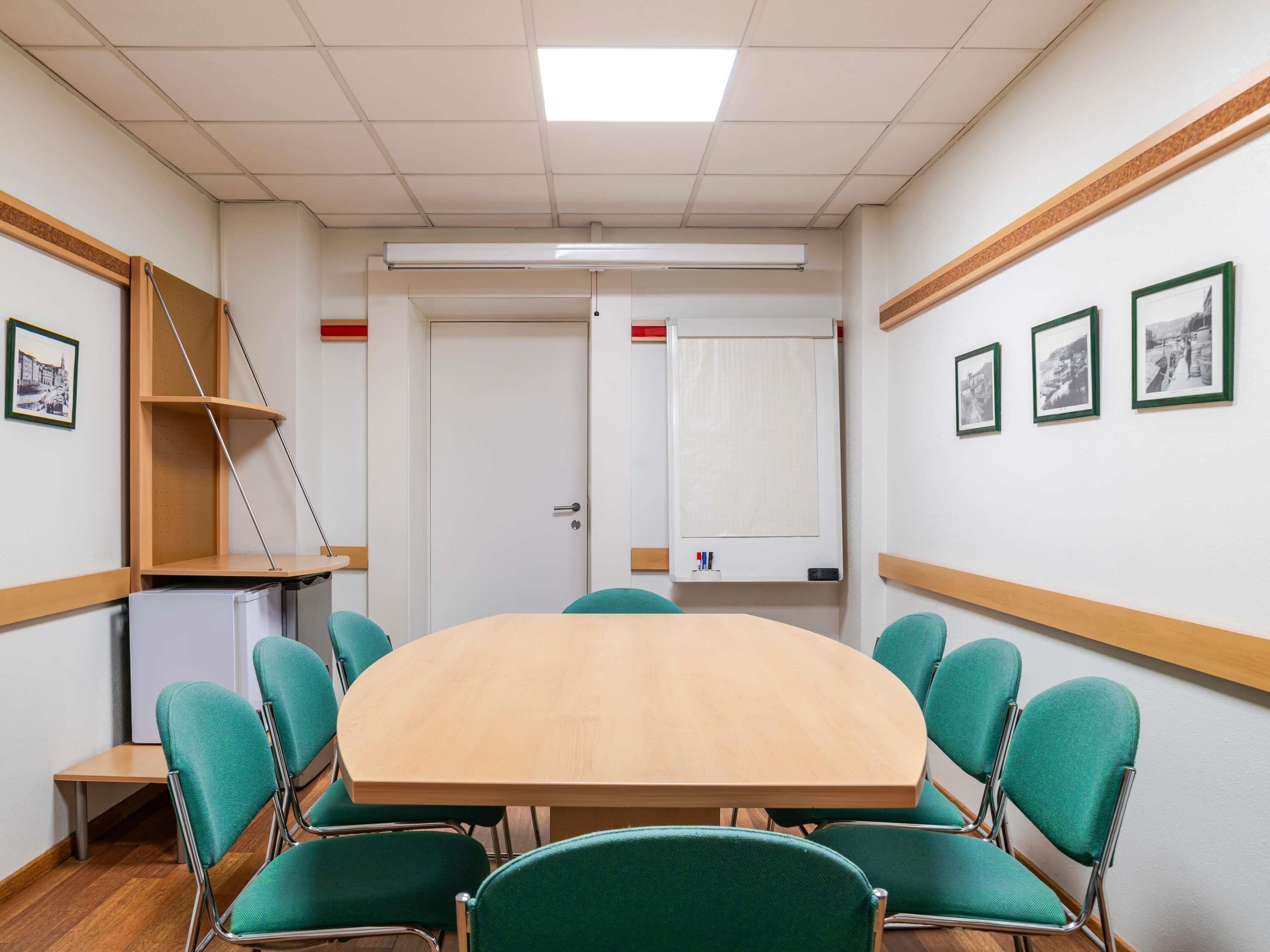 Un salón de conferencias con una mesa redonda, sillas verdes, una pizarra y cuadros en las paredes.