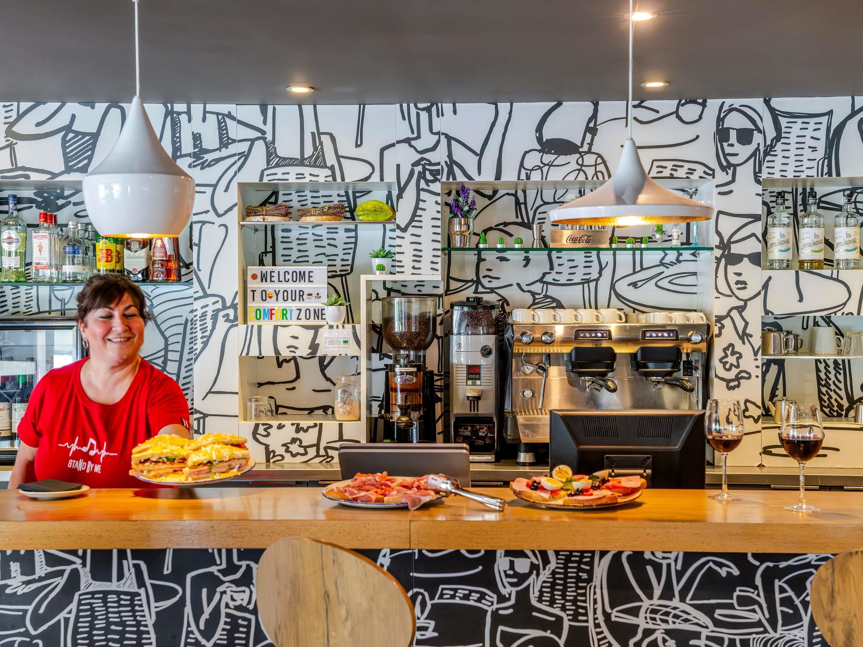 A bar area with a coffee machine, a sign that reads 'WELCOME TO YOUR COMFORT ZONE,' and a person serving food.