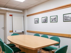 Un salón de conferencias con una gran mesa ovalada, sillas verdes, una pizarra y cuatro cuadros en la pared.