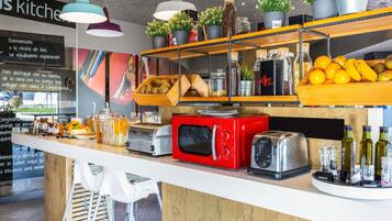 Una cocina con mostrador de madera, varios electrodomésticos, incluyendo un microondas rojo y un tostador, y estantes con frutas y frascos.
