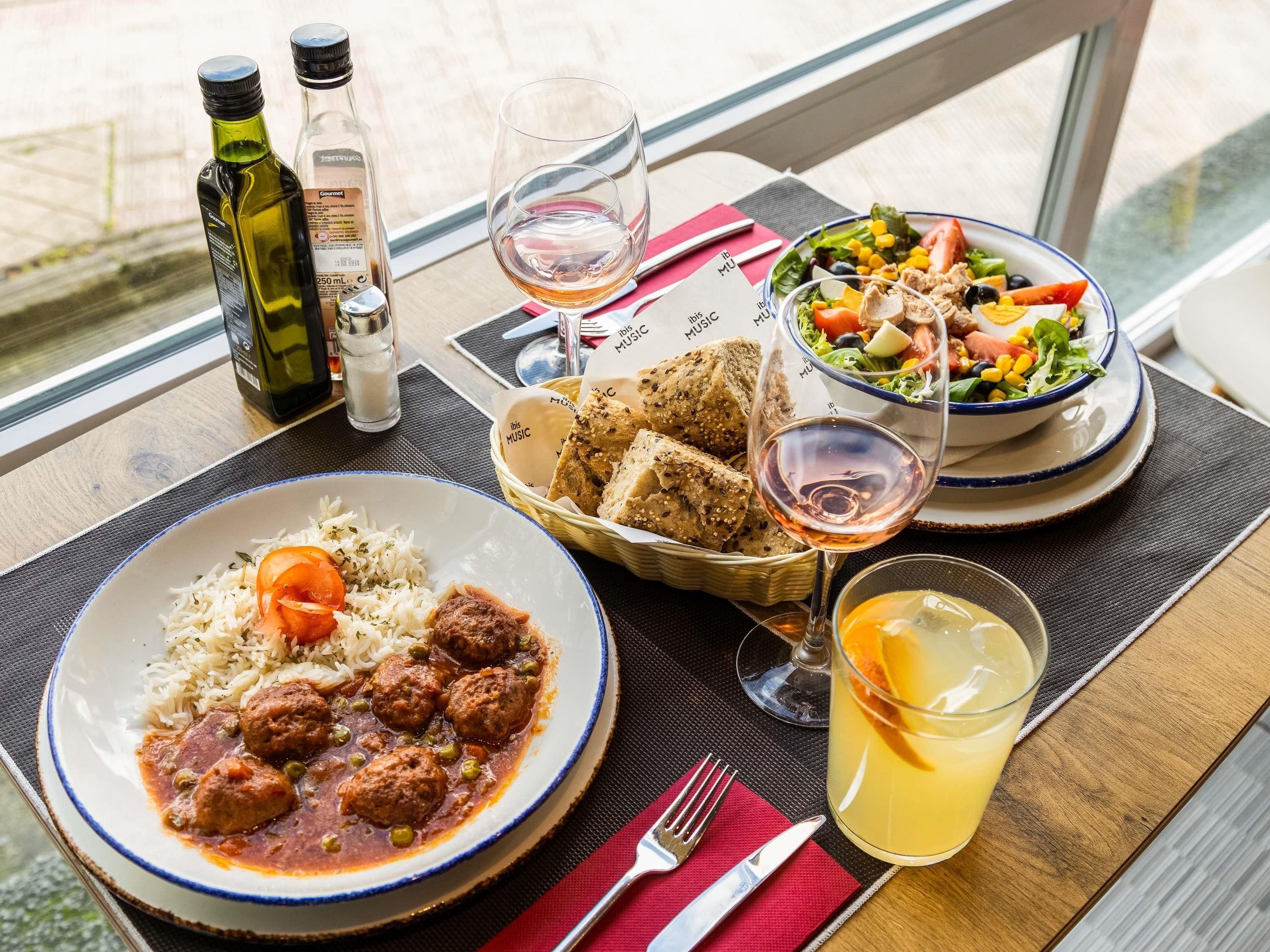Una mesa con un plato de albóndigas con arroz, ensalada, pan y un vaso de jugo de naranja.