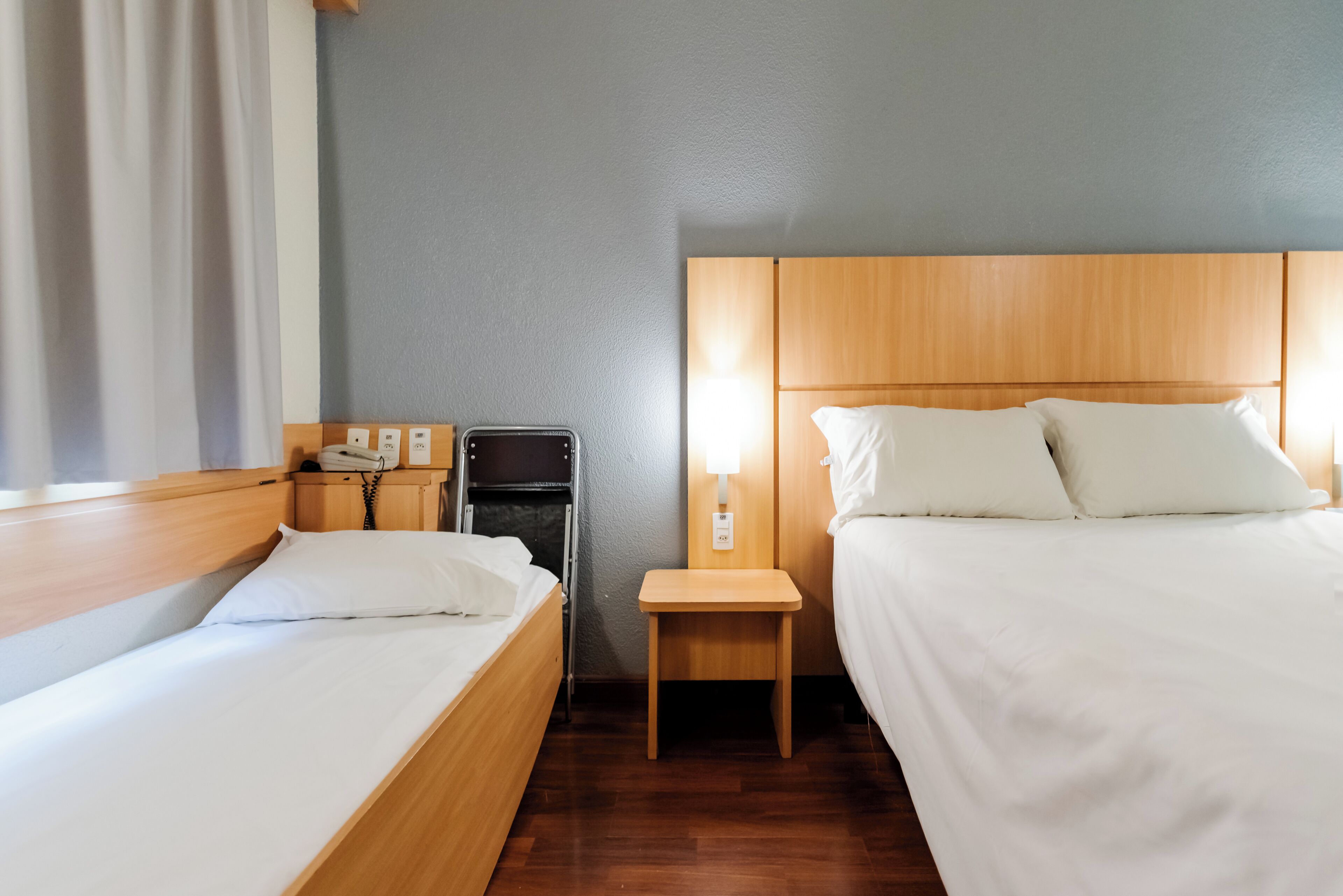 Una habitación de hotel con dos camas, una mesita de noche con teléfono, lámpara y un armario pequeño.