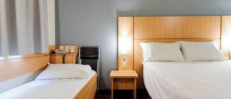 Una habitación de hotel con dos camas, una mesita de noche con teléfono, lámpara y un armario pequeño.