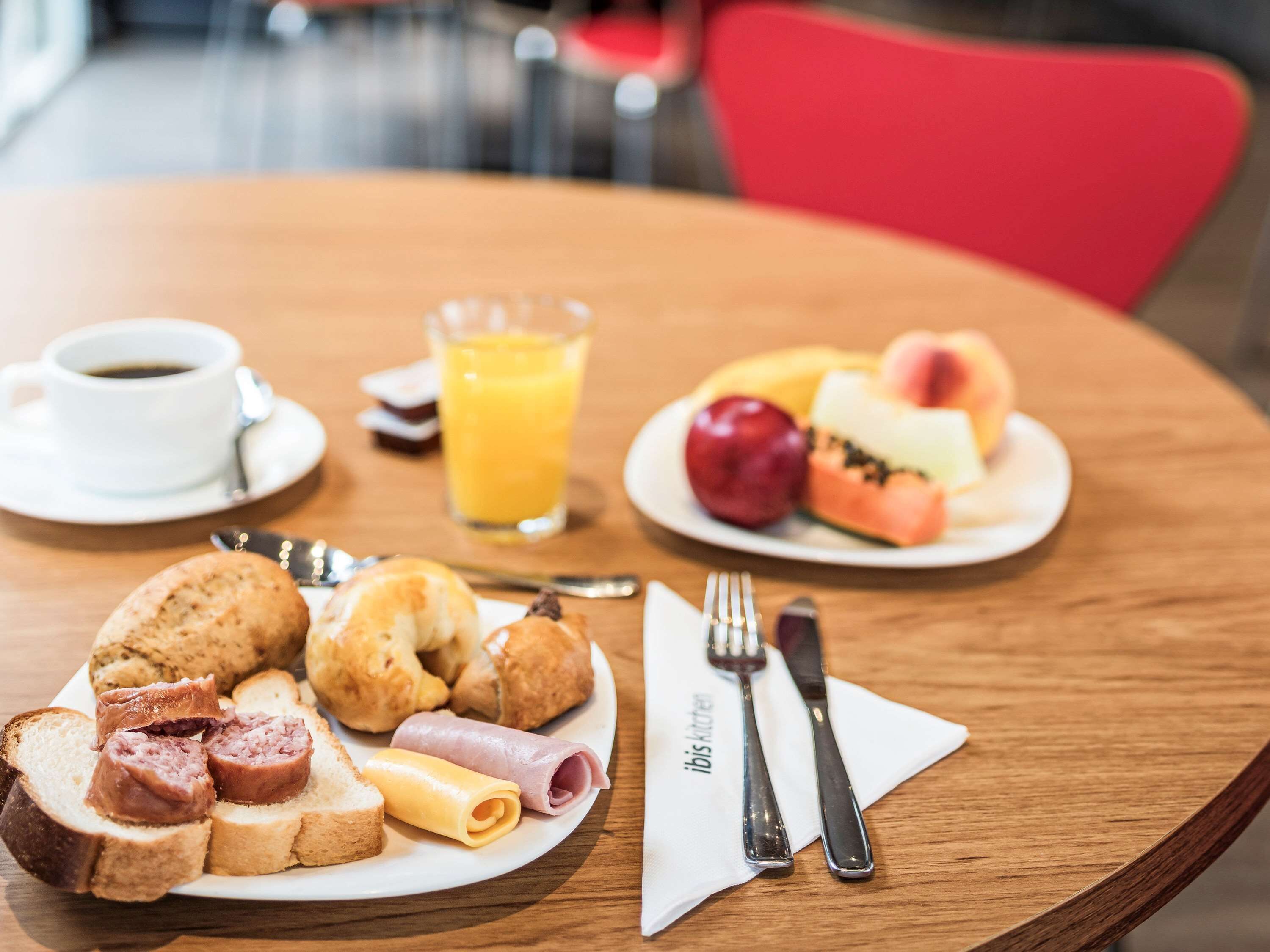 A breakfast setting with a plate of croissants, ham, cheese, and bread, a cup of coffee, a glass of orange juice, and a plate of fruit.