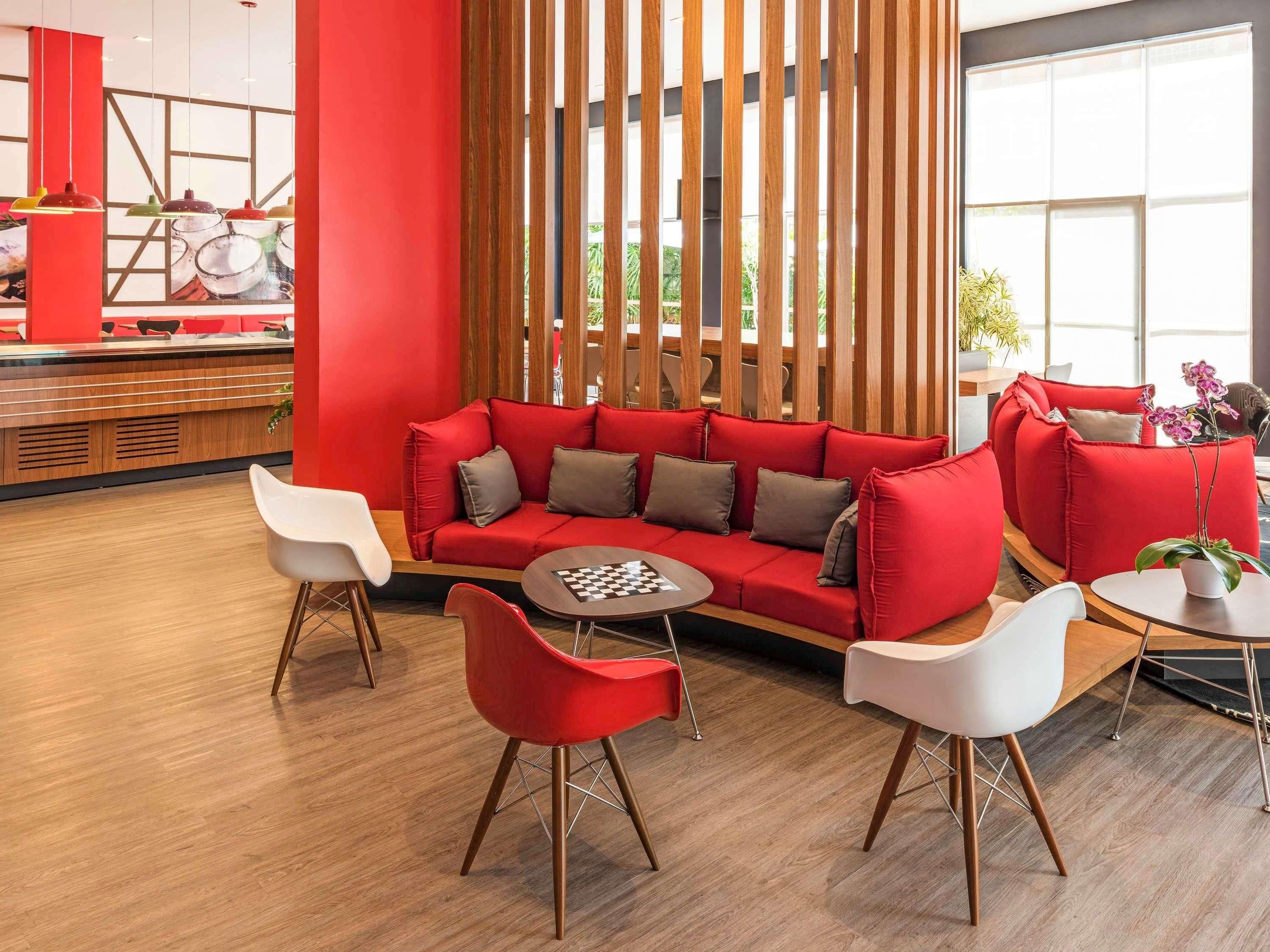 Un interior moderno con un sofá rojo, sillas blancas y un separador de madera.