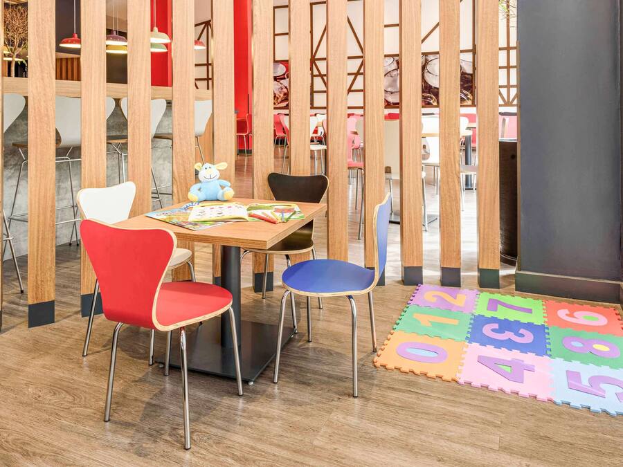A children's play area with a wooden partition, a table with books and toys, and colorful floor mats.