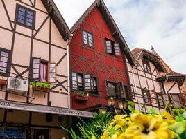 Un edificio tradicional con entramado de madera, fachada roja y numerosas ventanas, incluyendo una tienda con un cartel visible.