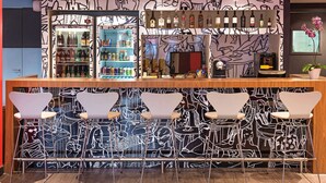 A bar area with a graffiti-style wall, a variety of liquor bottles, and five bar stools. - ibis Blumenau (Blumenau)