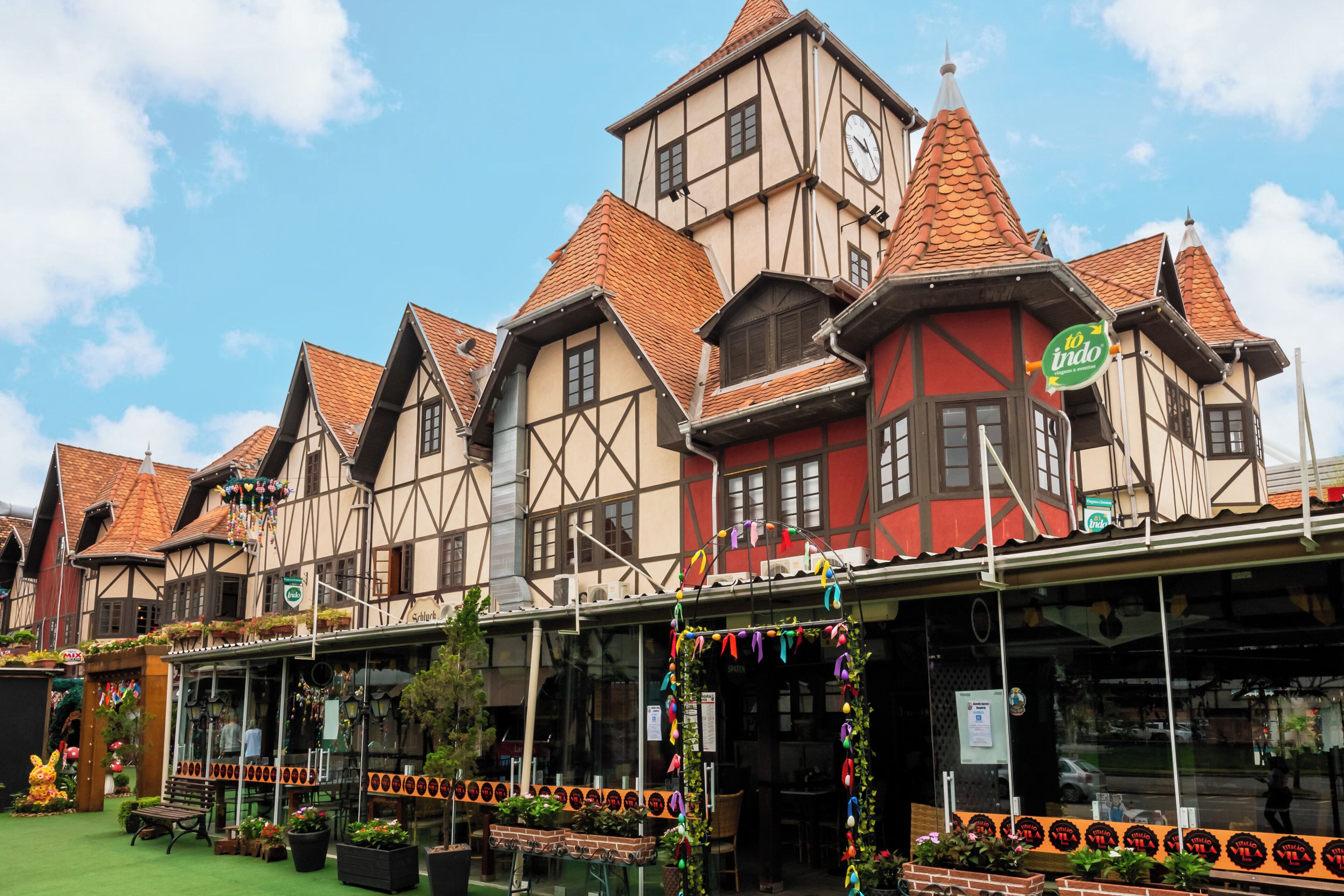 Un bâtiment traditionnel à colombages, doté d’une tour horlogée, d’un espace extérieur couvert aménagé en terrasse et d’une enseigne indiquant « Indo ».