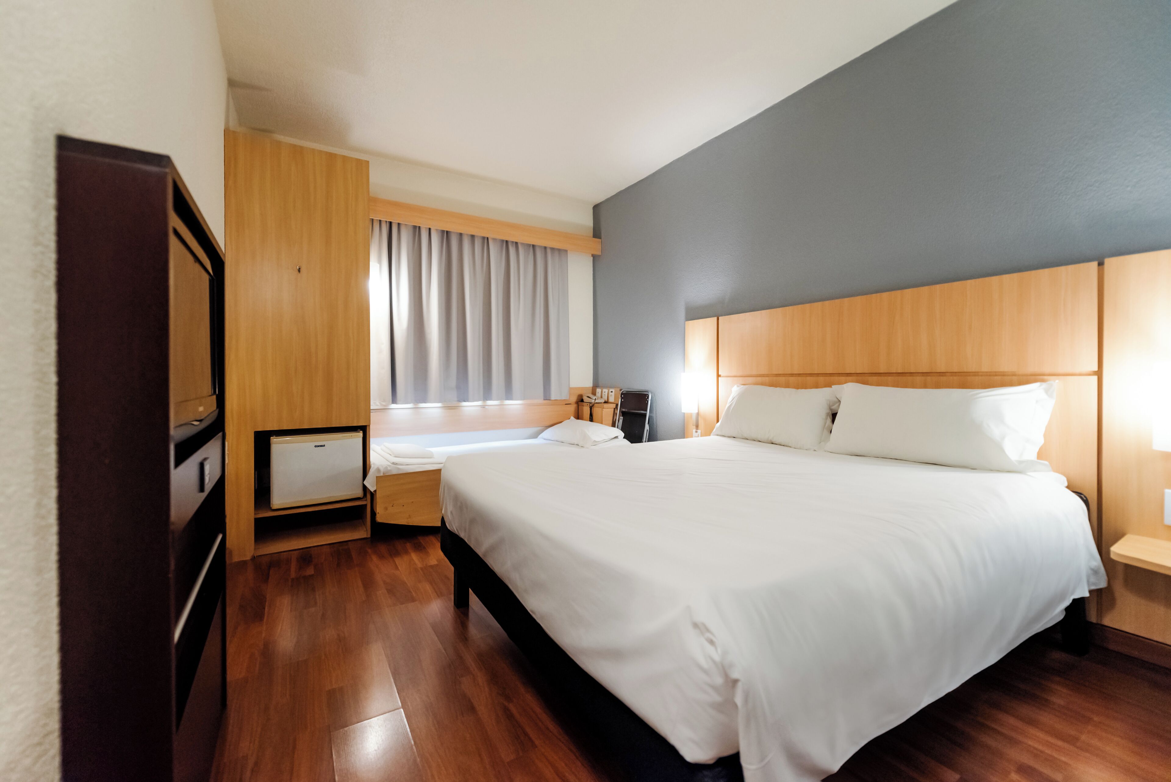 Een hotelkamer met een groot bed, een nachtkastje, een bureau en een raam met gordijnen.