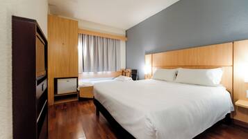 Een hotelkamer met een groot bed, een nachtkastje, een bureau en een raam met gordijnen.