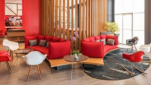 A modern lounge area with red sofas, a wooden partition, and a large window providing natural light. - ibis Blumenau (Blumenau)
