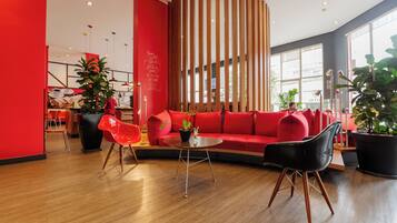 Un interior moderno con un sofá rojo, sillas negras y rojas, un pilar de madera y una planta en maceta.