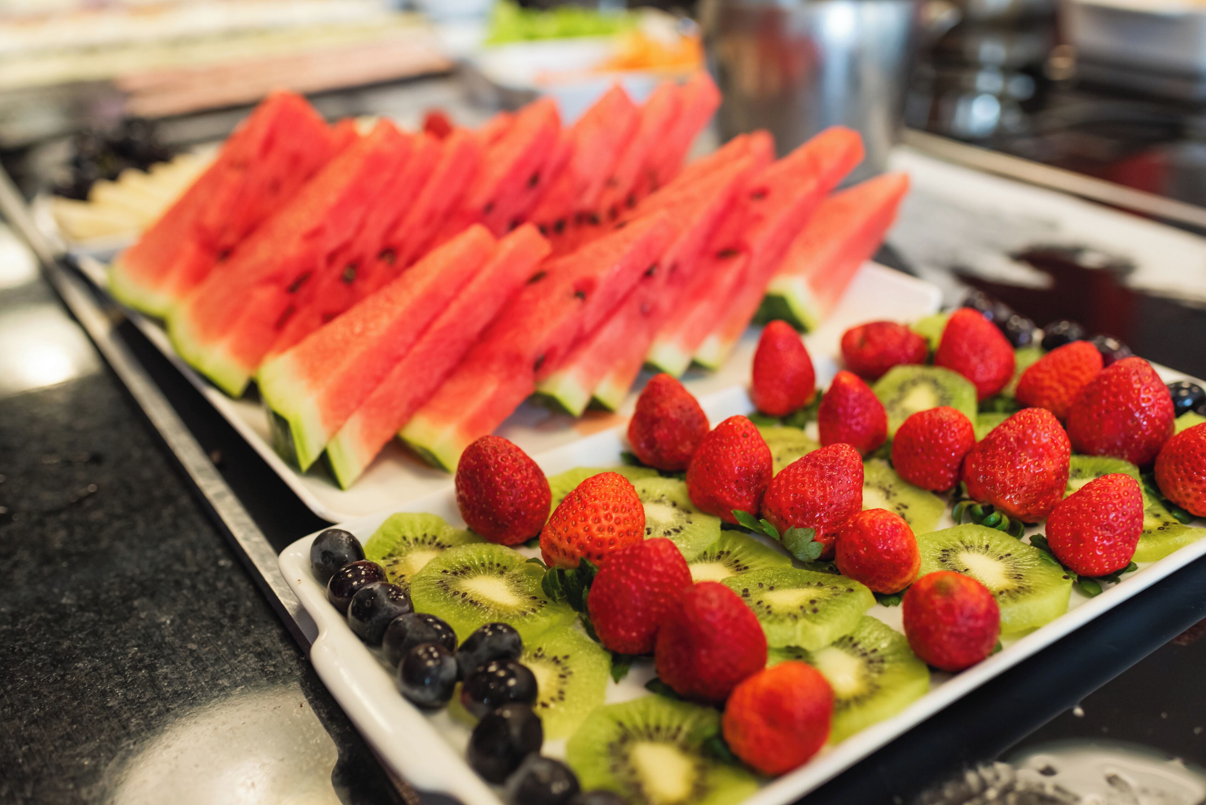 A buffet with sliced watermelon, strawberries, and kiwi arranged on a tray.