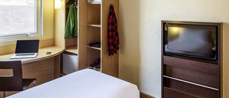 Habitación de hotel compacta con cama, escritorio con computadora portátil, televisión y armario con estantes.