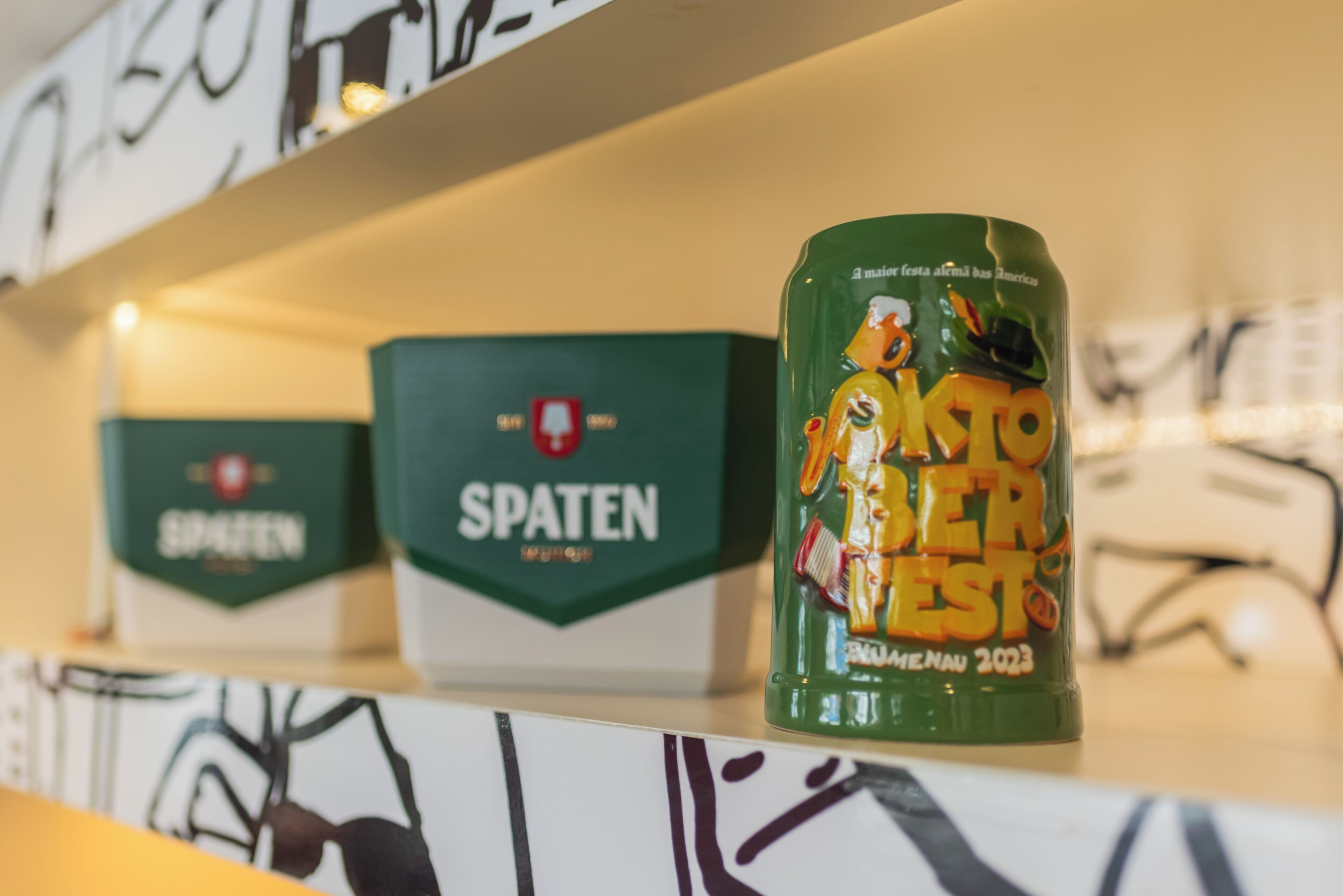 Ein Regal mit Kisten mit dem Aufdruck 'SPATEN' und einem Behälter mit der Aufschrift 'KOTTO BIER' und 'HERAUSFORDERUNG 2023'.