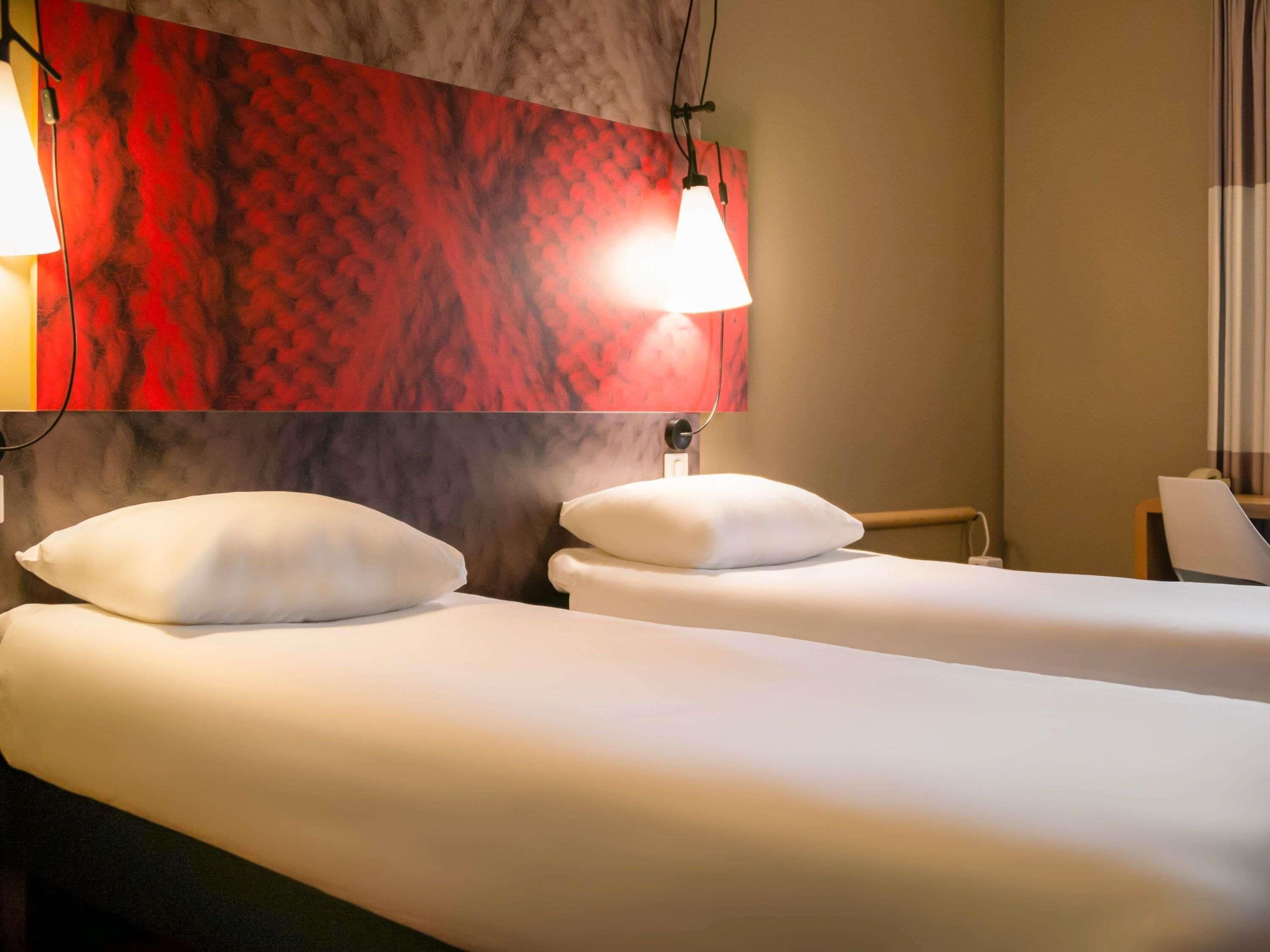 Una habitación de hotel con dos camas, un muro con estampado rojo y una lámpara.