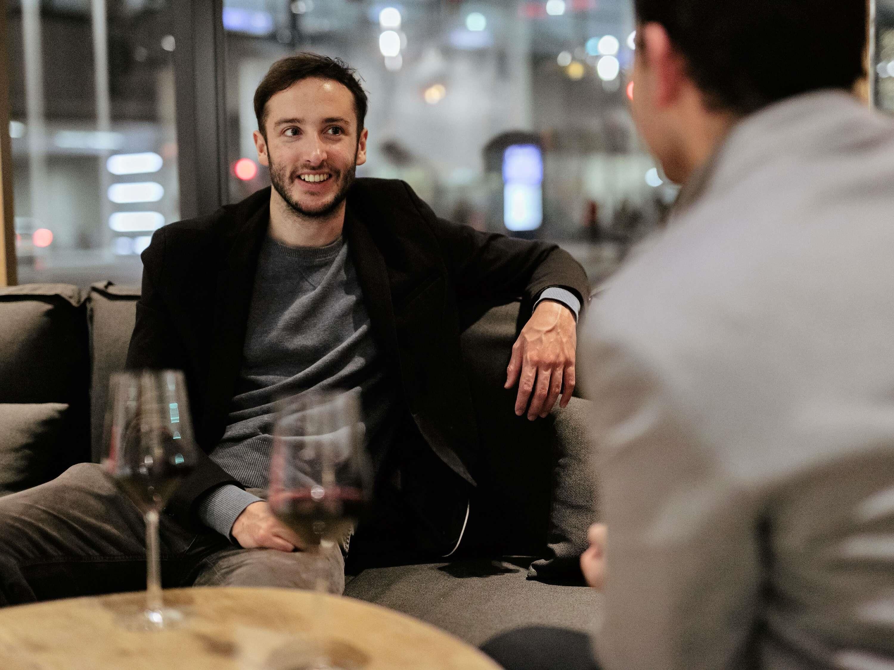 Une personne assise sur un canapé, avec un verre de vin posé sur une table devant elle.