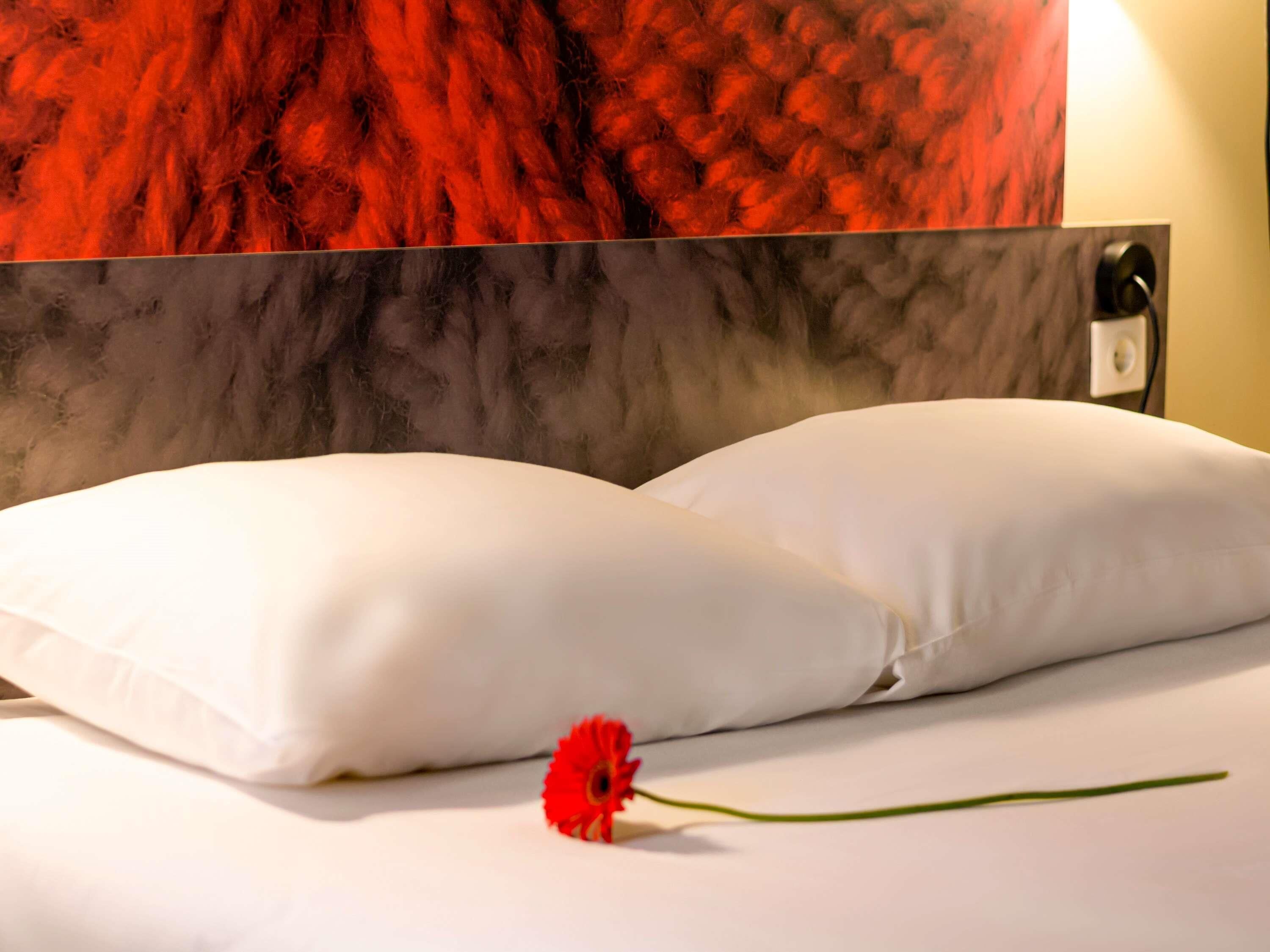 A bed with white pillows and a red flower on the bed.