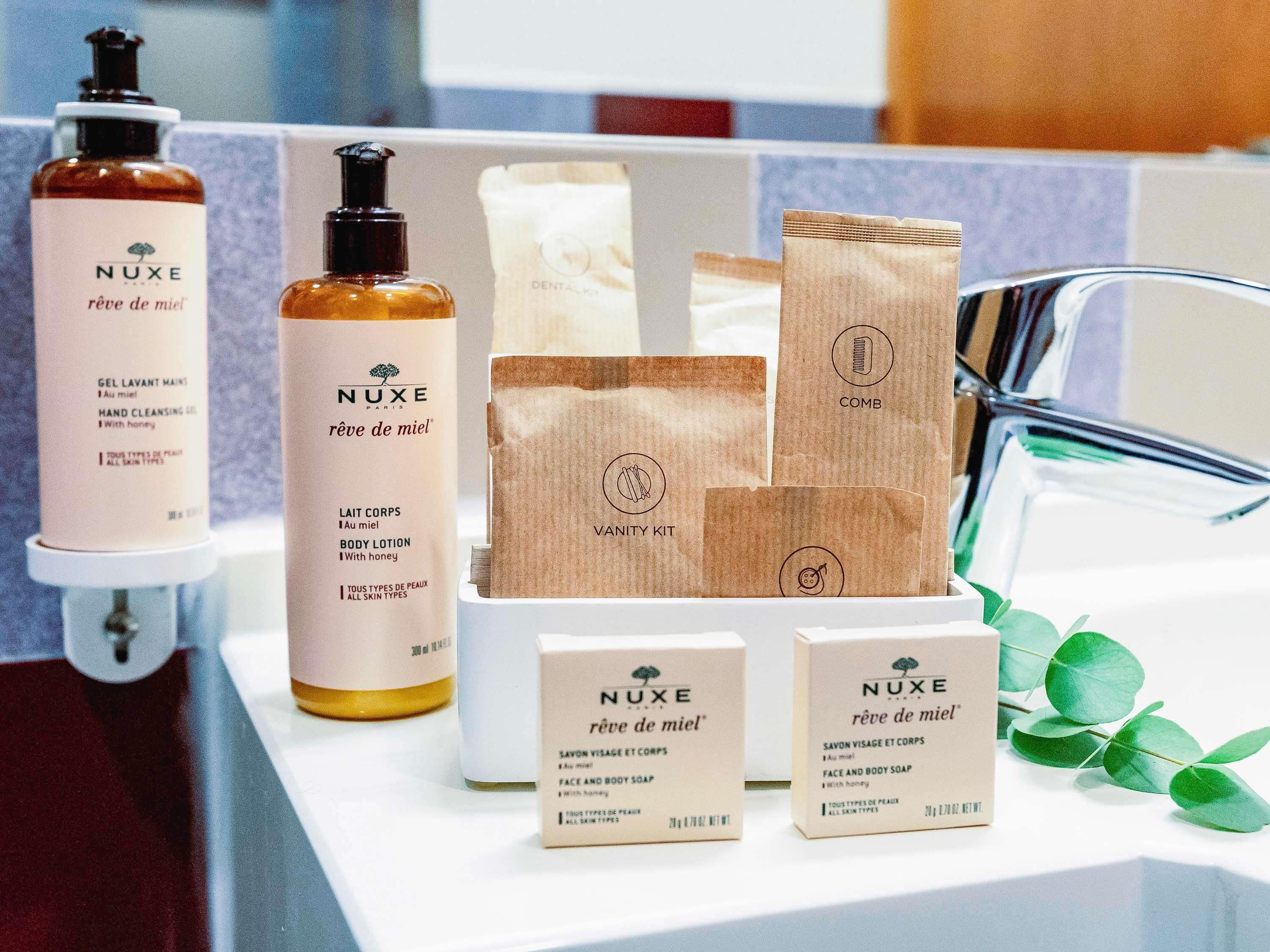 Una encimera de baño con productos de cuidado de la piel NUXE, incluyendo un gel limpiador de manos, loción corporal y un neceser.
