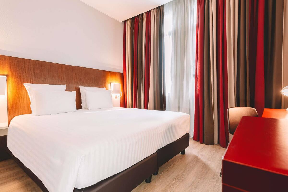 A hotel room with a bed, bedside lamps, a desk, and a chair.