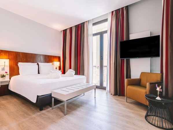 Une chambre d’hôtel avec un lit, une table de chevet, une lampe, une télévision, une chaise et une petite table agrémentée de fleurs.