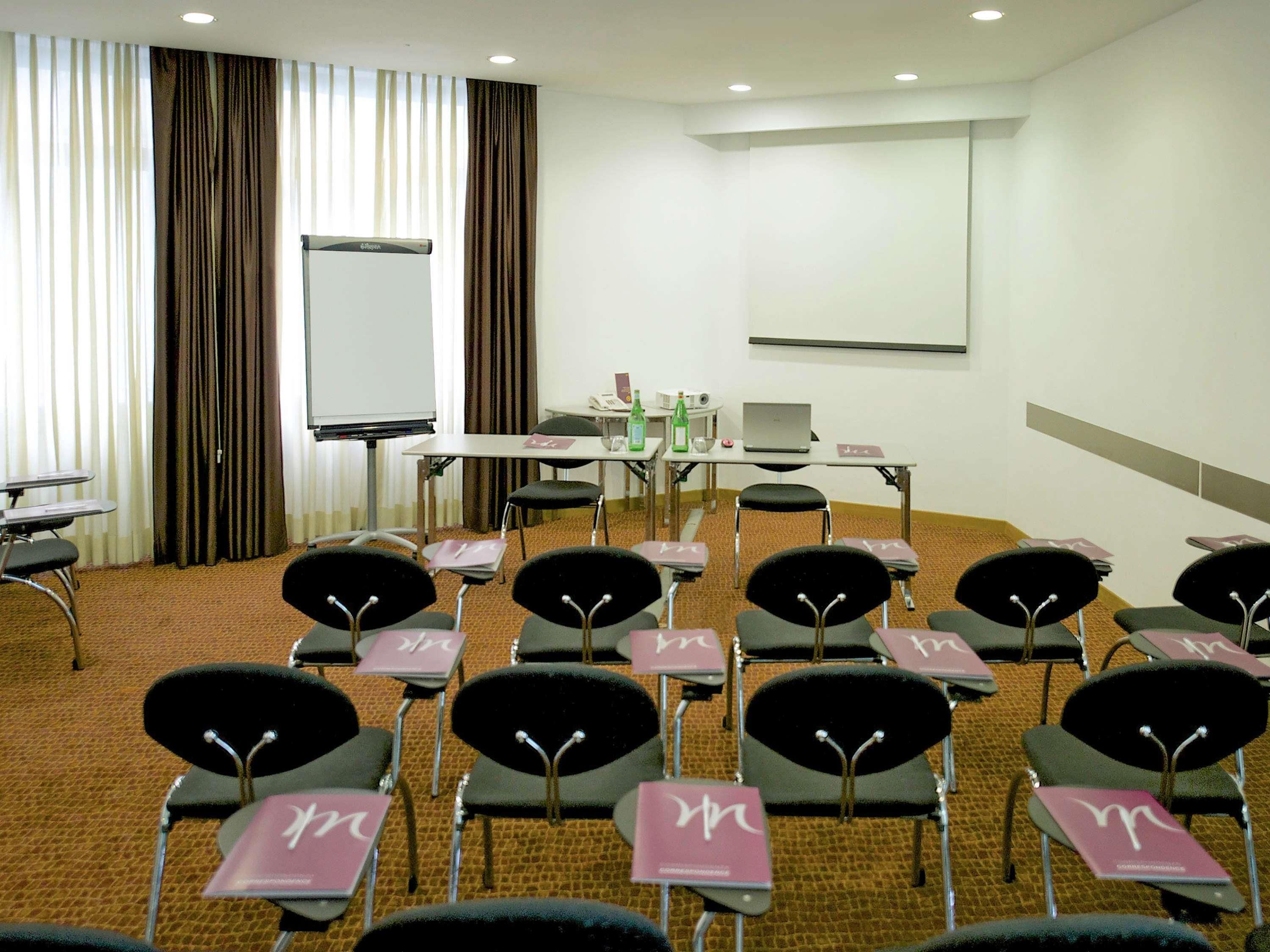 A conference room with a whiteboard, a projector screen, a laptop, and multiple chairs with name cards.
