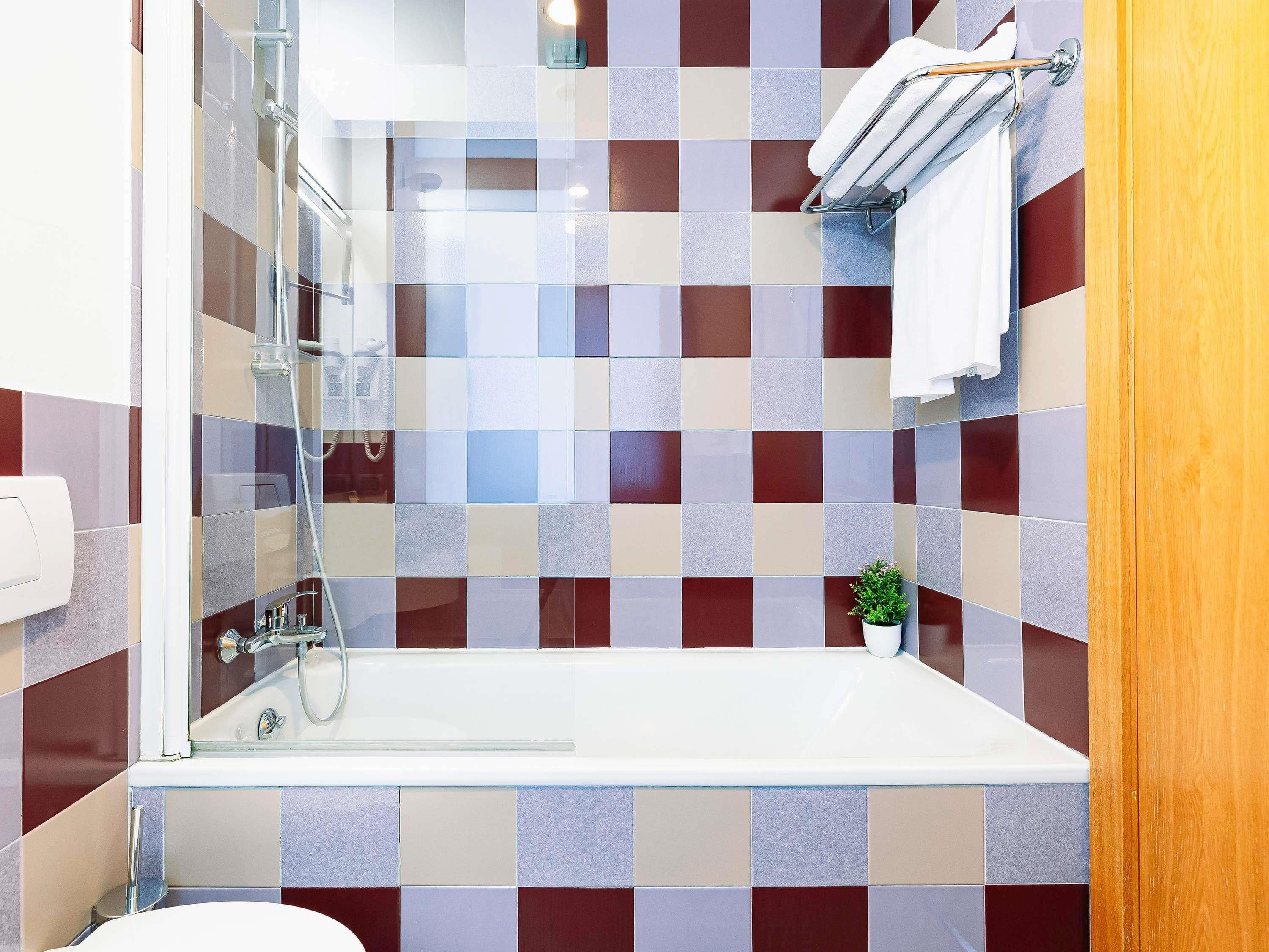 A modern bathroom with a glass-enclosed shower, a white bathtub, and a checkered tile wall.