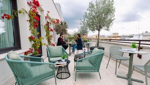 Um terraço com móveis de vime verde, uma pequena mesa redonda e plantas em vasos.