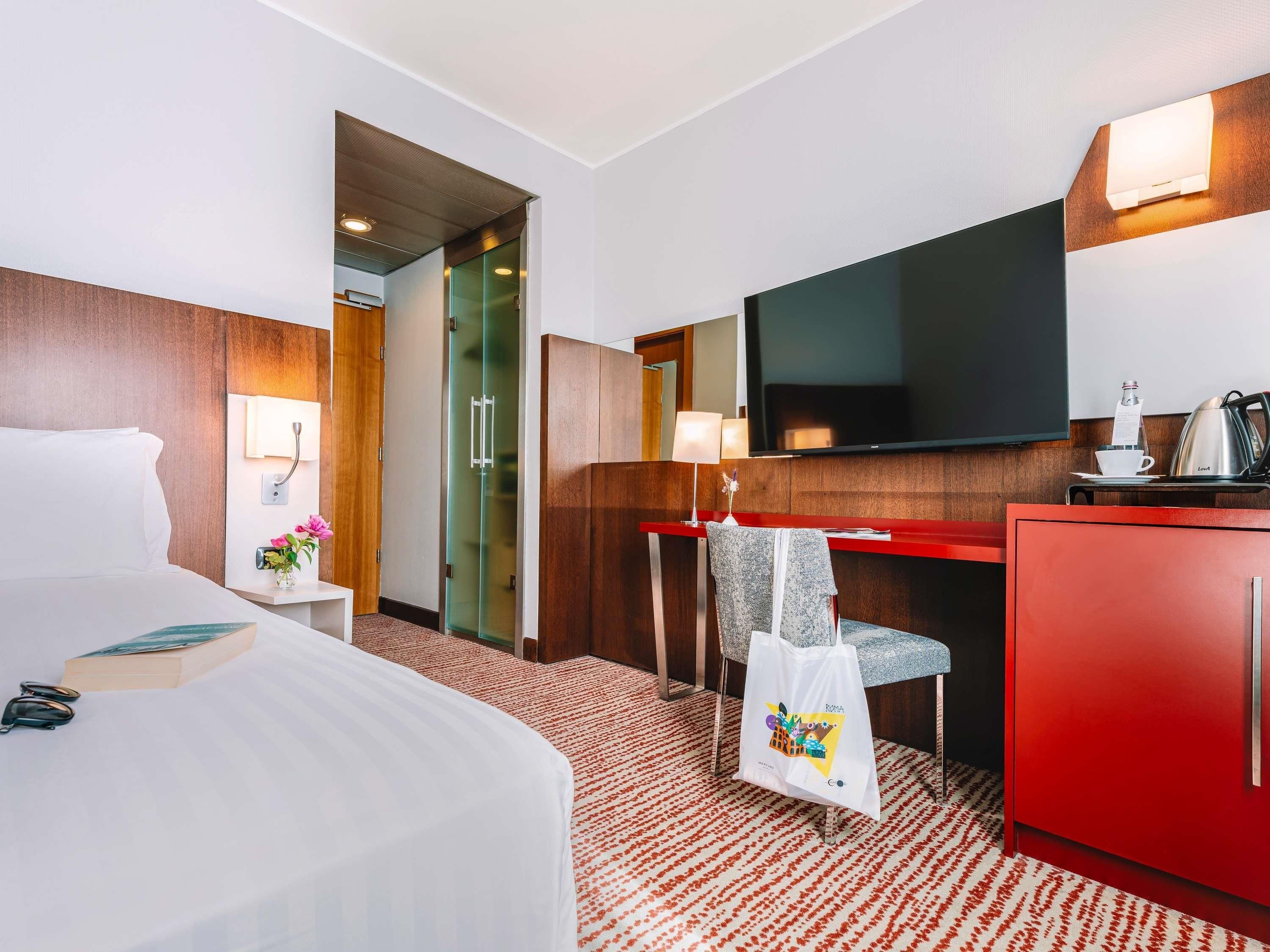 Ein Hotelzimmer mit Bett, Schreibtisch, Fernseher, Minibar und einem roten Schrank.