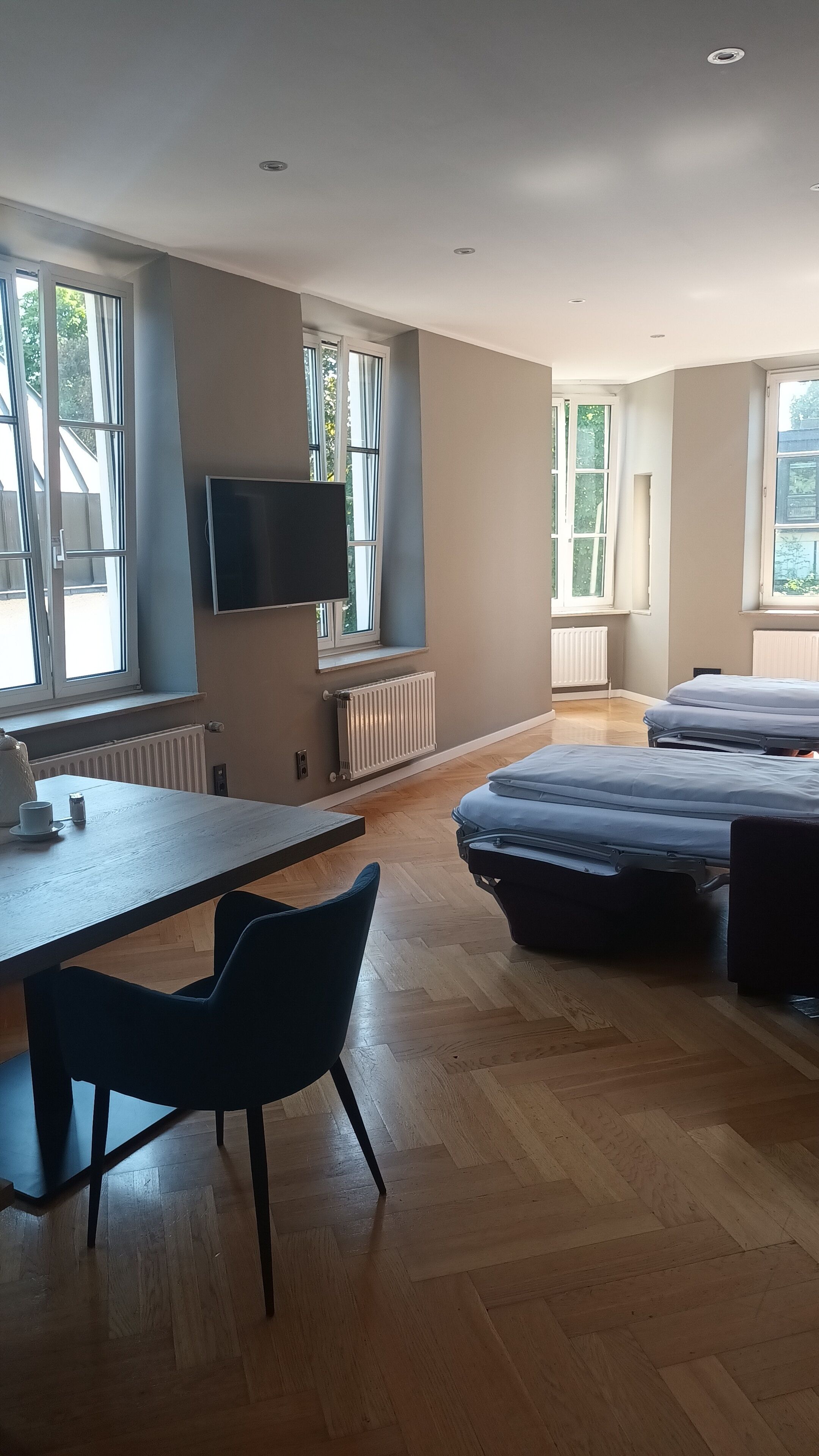 A modern room with a wooden floor, a desk with a chair, a bed, and a TV mounted on the wall.