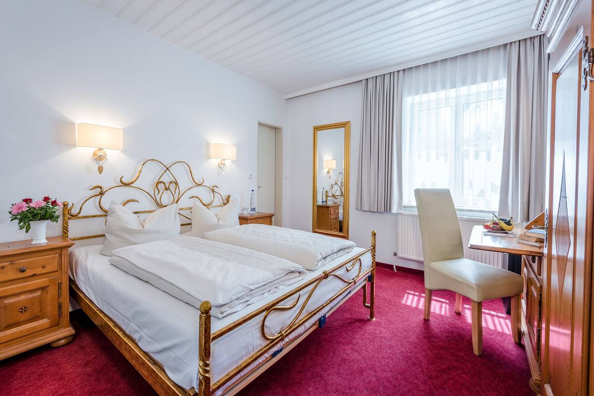 A hotel room with a large bed, a desk, a chair, and a mirror.