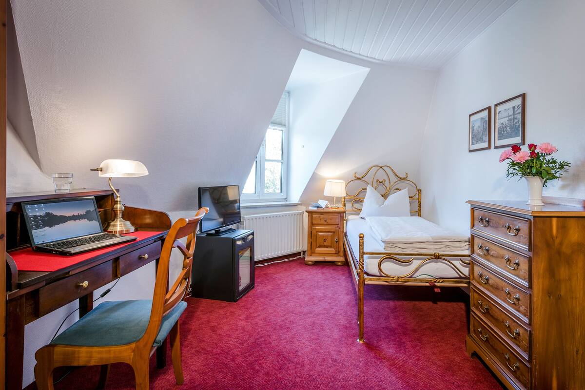 A bedroom with a desk, laptop, television, and a bed with a dresser.