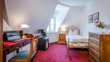A bedroom with a desk, laptop, television, and a bed with a dresser.