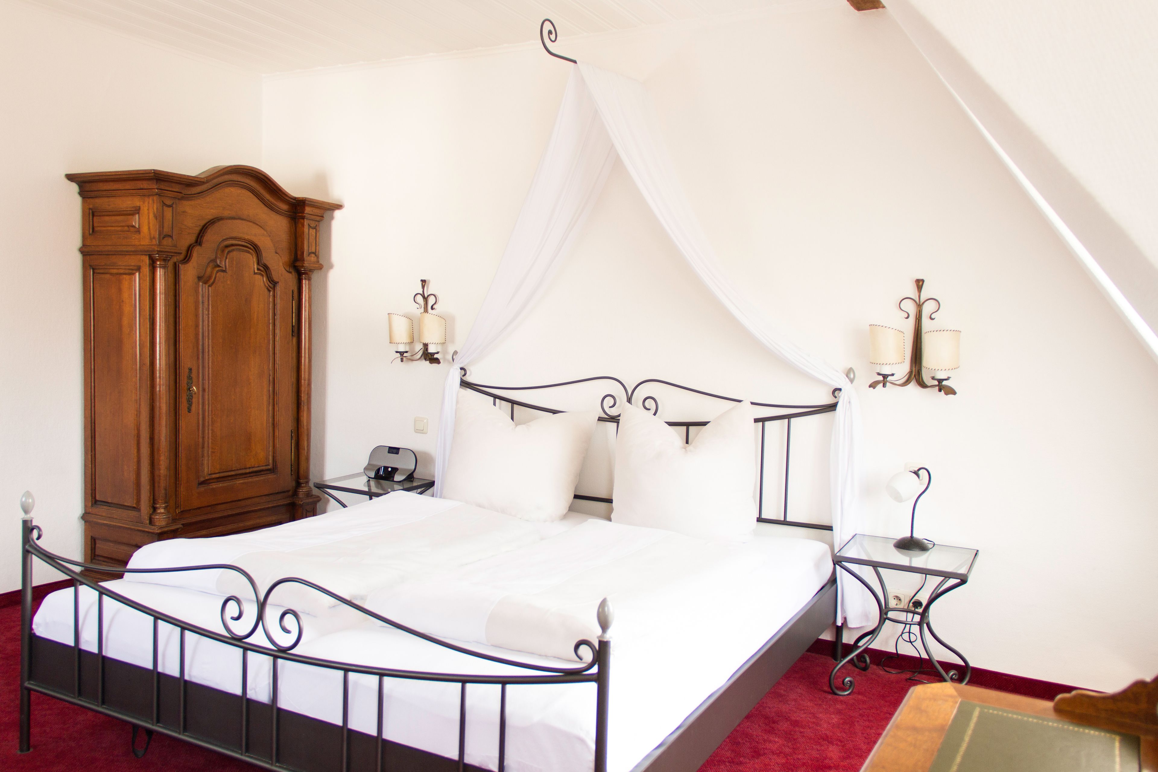Un dormitorio con una cama con dosel, un armario de madera, dos mesitas de noche con lámparas y una alfombra roja.
