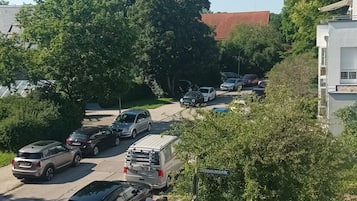 Un estacionamiento con varios coches, un edificio de techo rojo y una calle con peatones.
