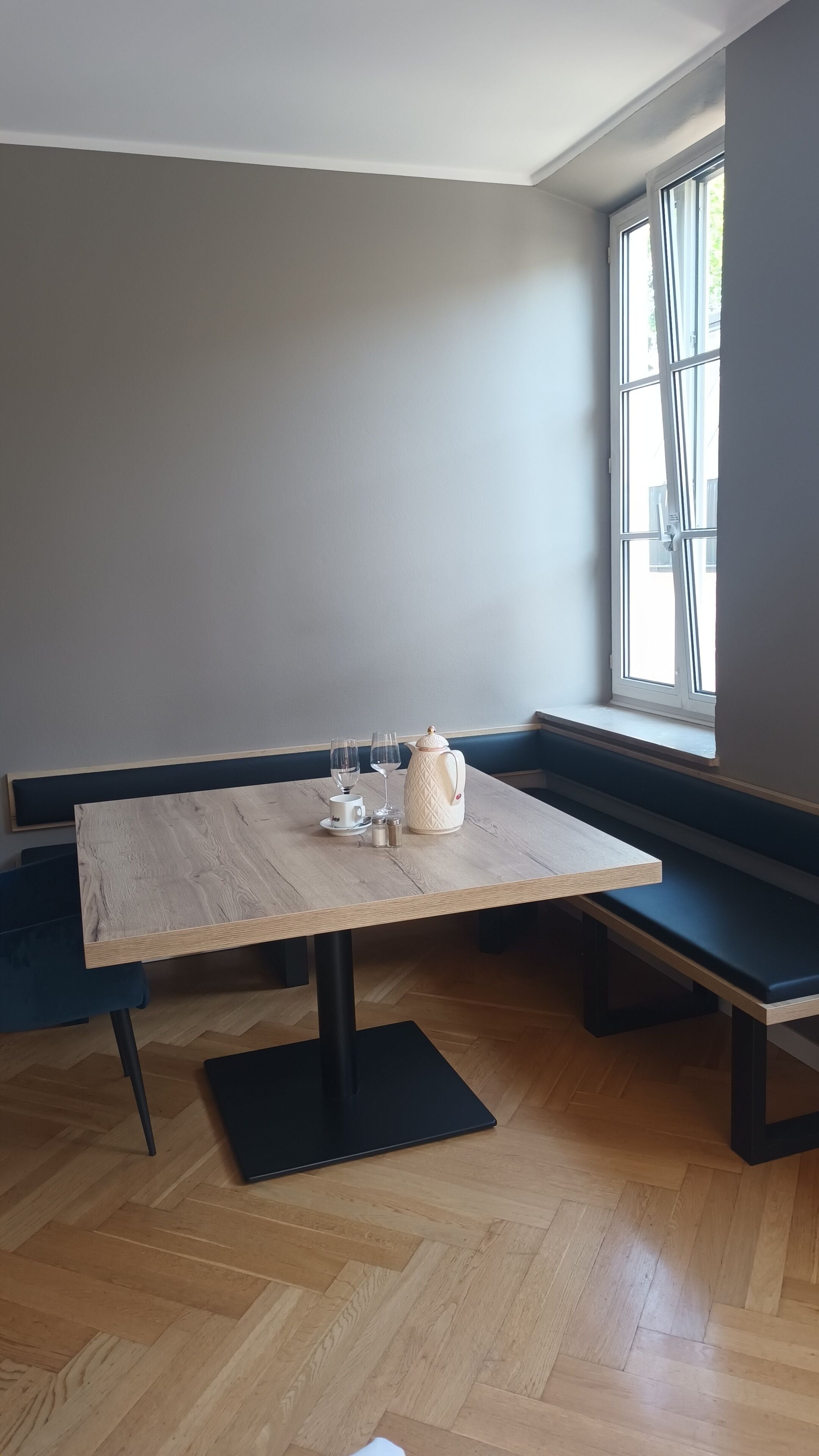 Una habitación de esquina con una mesa de madera, dos sillas, un banco y un ventanal.