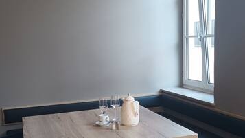 Una habitación de esquina con una mesa de madera, dos sillas, un banco y un ventanal.