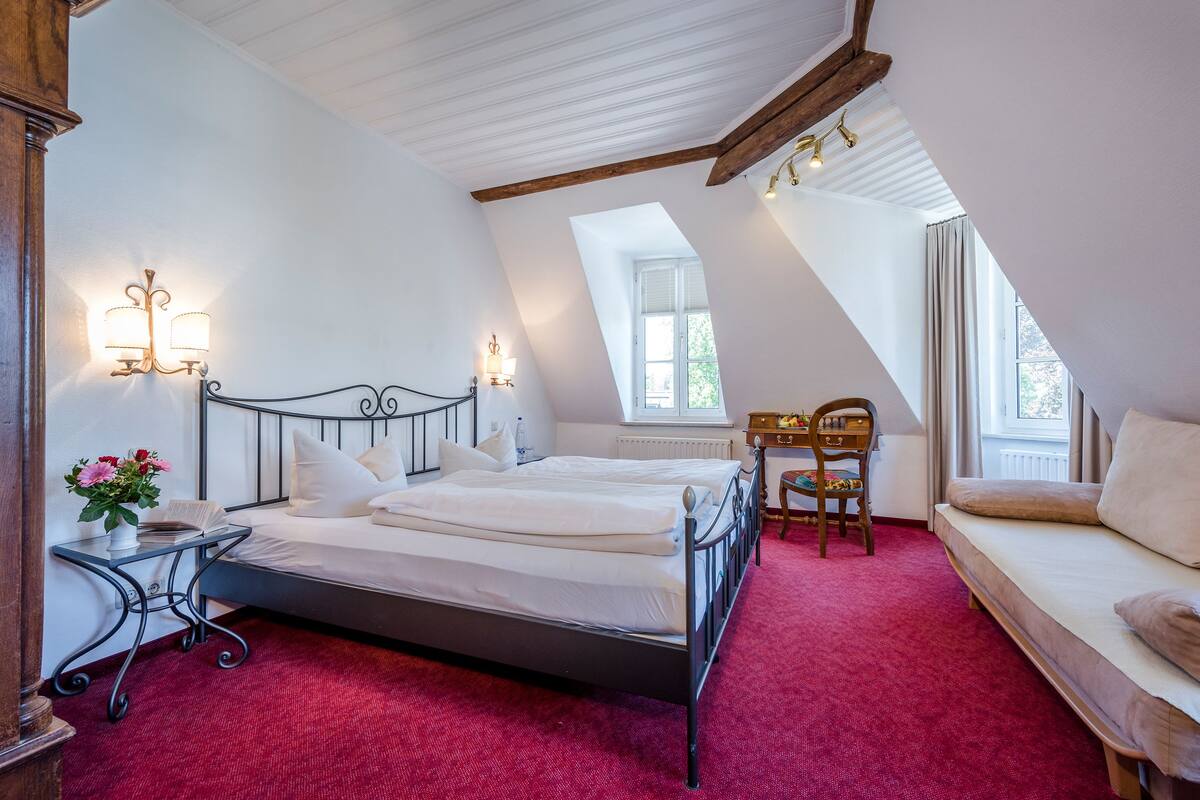 A bedroom with a bed, a desk, a chair, and a sofa.