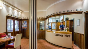A reception area with a curved counter labeled "Laimer Hof," a wooden bench, and a tiled floor. - Hotel Laimer Hof Nymphenburg Palace Munich (Munich)