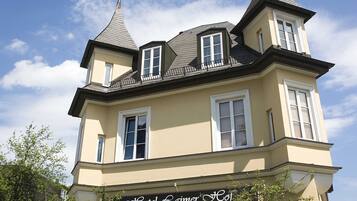 A two-story building with a sign reading "Hotel Lambert Hof". It features a steeply pitched roof, dormer windows, and a small balcony on the upper floor.
