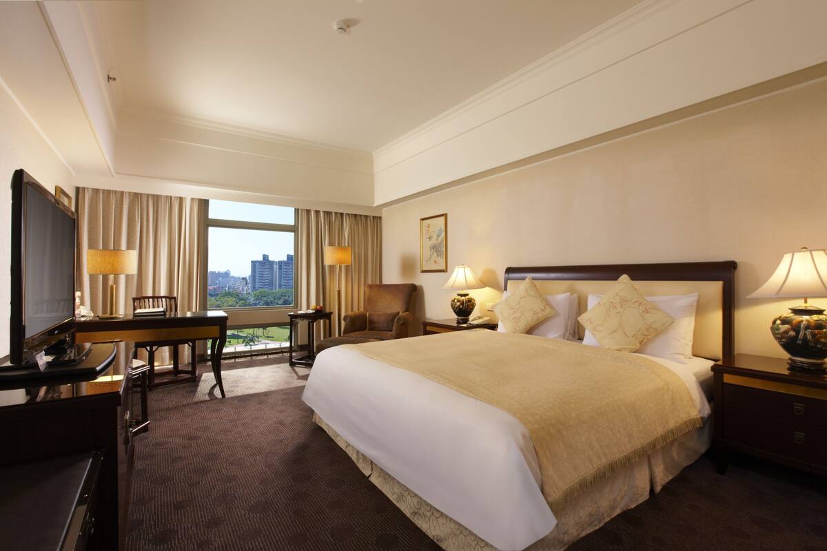 Hotelkamer met een groot bed, een bureau, een stoel, een televisie en een raam met uitzicht op de stad.