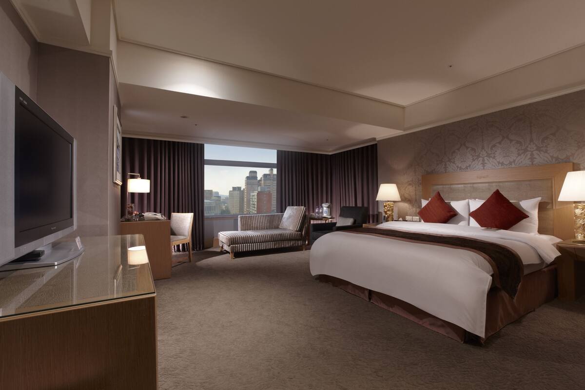 Een hotelkamer met een groot bed, een televisie, een bureau, een stoel en uitzicht op de stad.