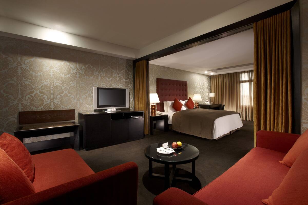 Een hotelkamer met een bed, een bureau met een televisie, een salontafel en rode meubels.