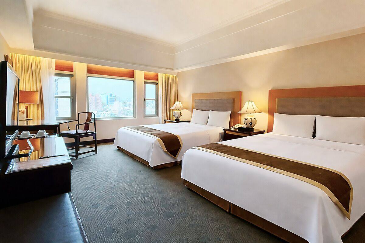 Hotelkamer met twee bedden, een bureau, een stoel en uitzicht op de stad.