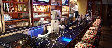 Zona de bar con una barra larga, estantes con botellas y una pantalla de televisión.