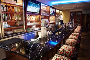 Eine Bar mit einer langen Theke, Regalen voller Flaschen und einem Fernseher.