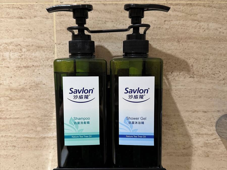Two bottles of Savlon shampoo and shower gel on a black wall-mounted dispenser.