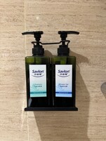Dos botellas de champú y gel de ducha Savlon sobre un dispensador montado en una pared negra.